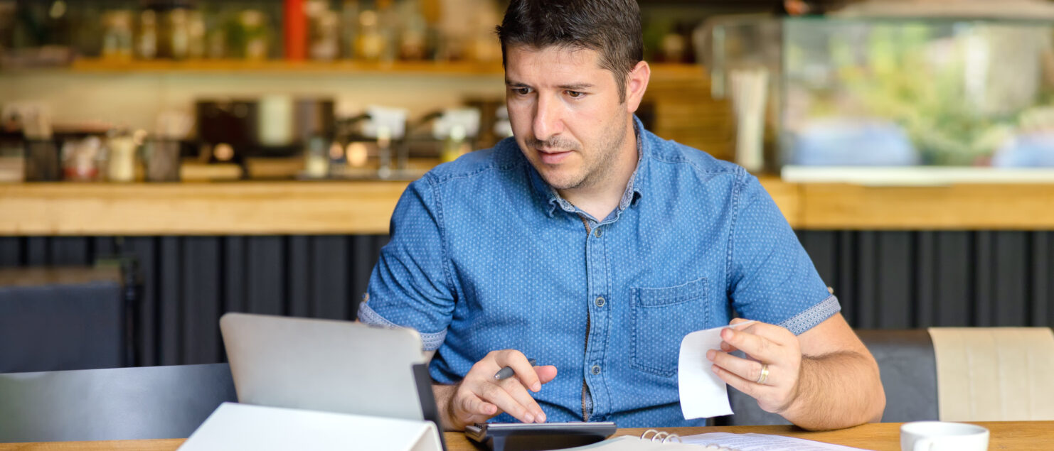 A business owner adds up receipts using a calculator and an ipad.