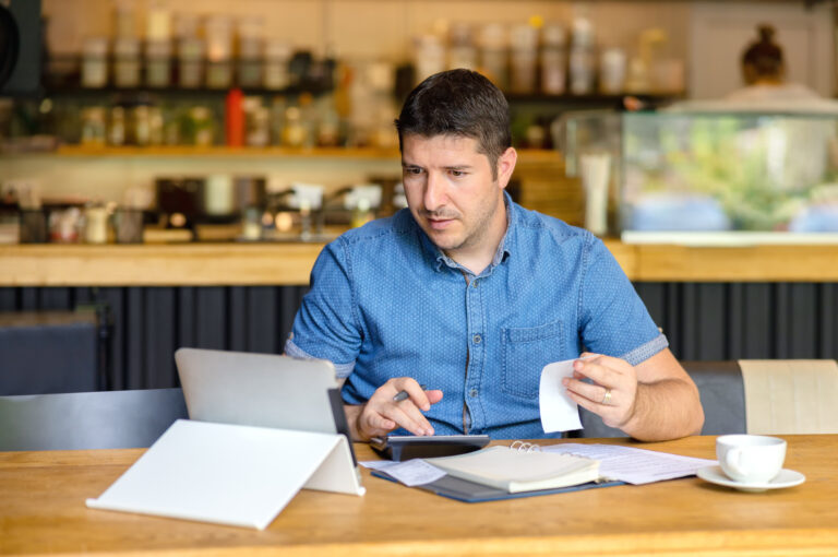 A business owner adds up receipts using a calculator and an ipad.