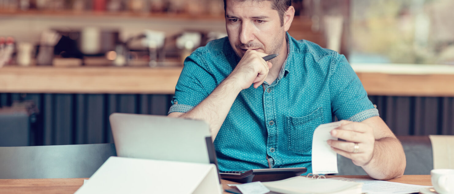 A restaurant owner sits in front of his laptop holding a receipt.