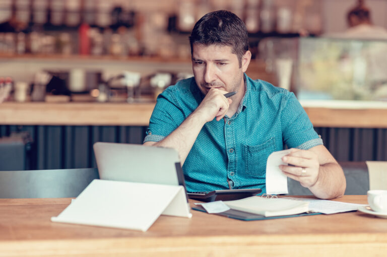 A restaurant owner sits in front of his laptop holding a receipt.