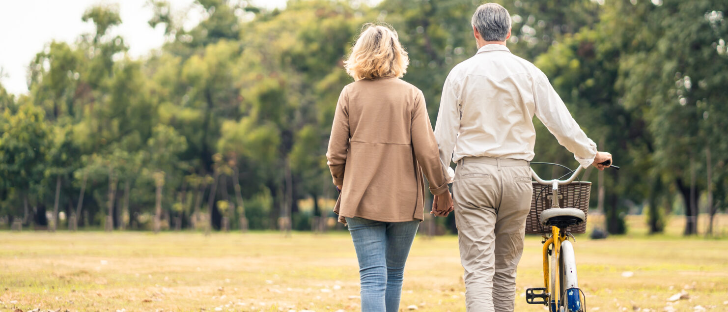 A couple walking through a park and pushing a bike.