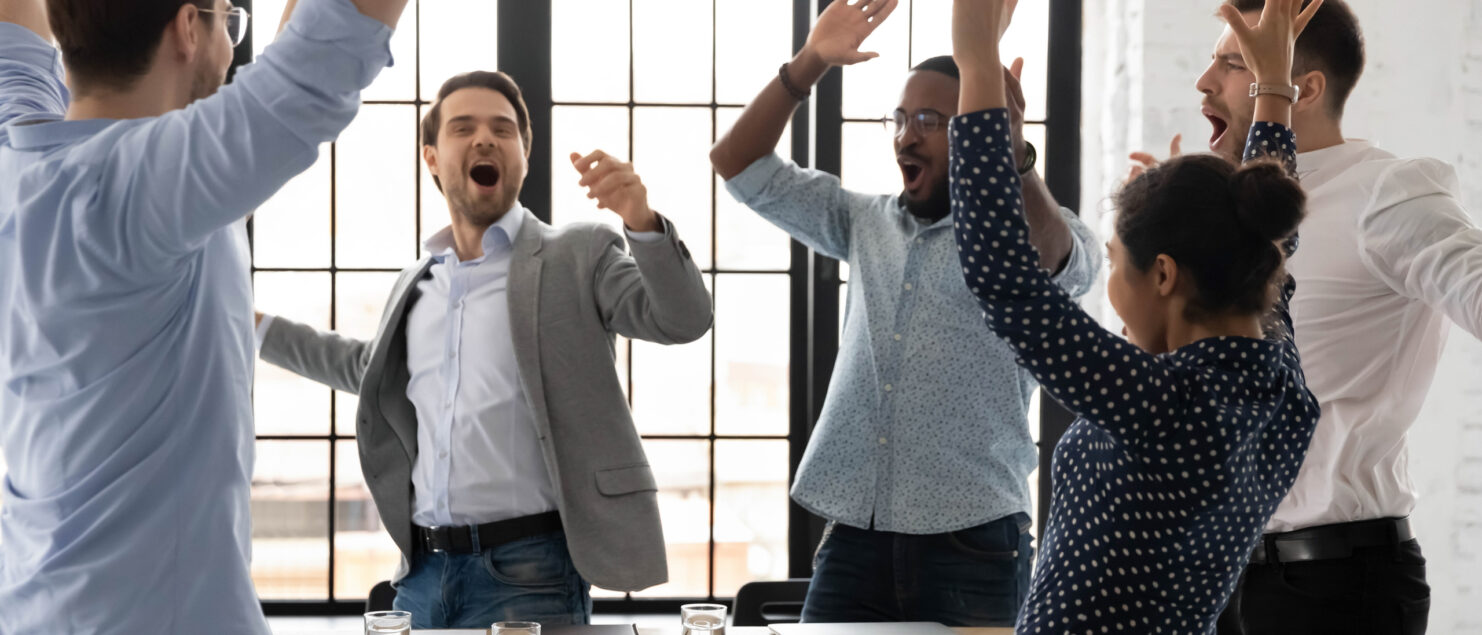 A group of employees jump up from their table in celebration