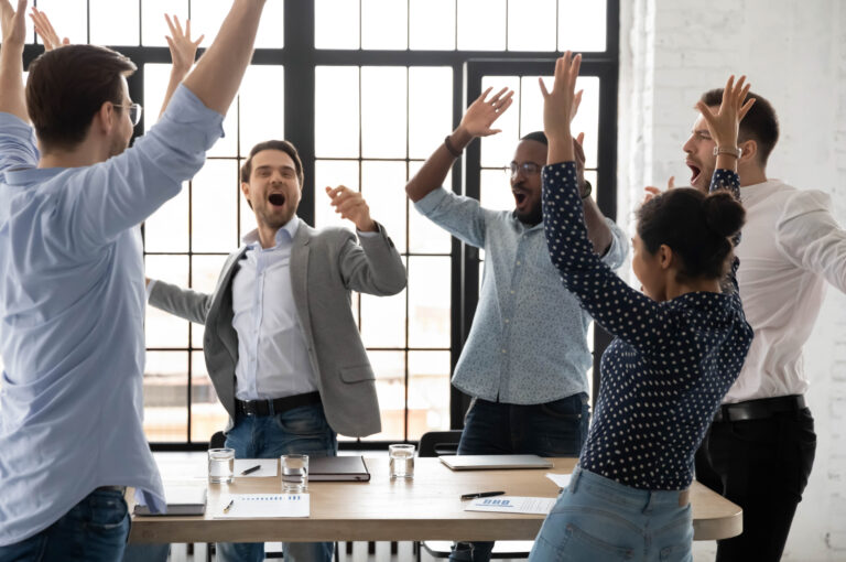 A group of employees jump up from their table in celebration