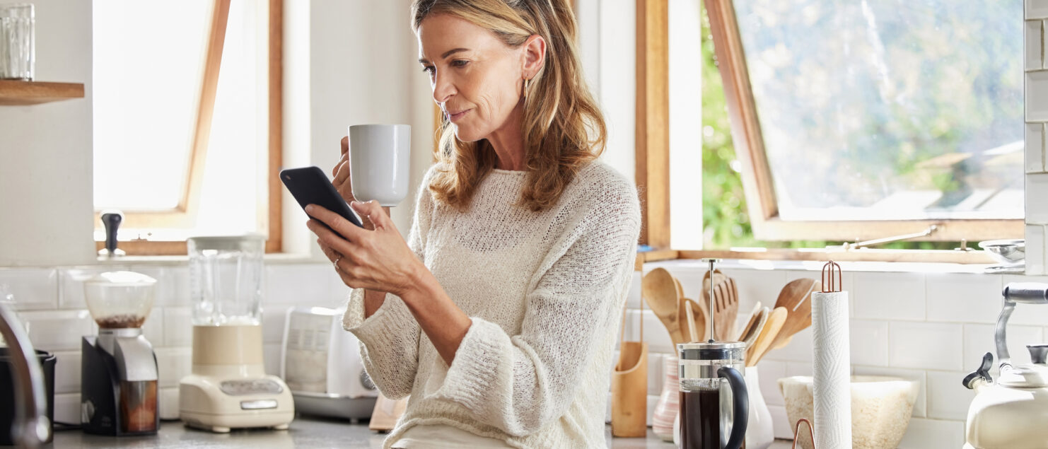 A woman drinking a coffee while looking at her phone.