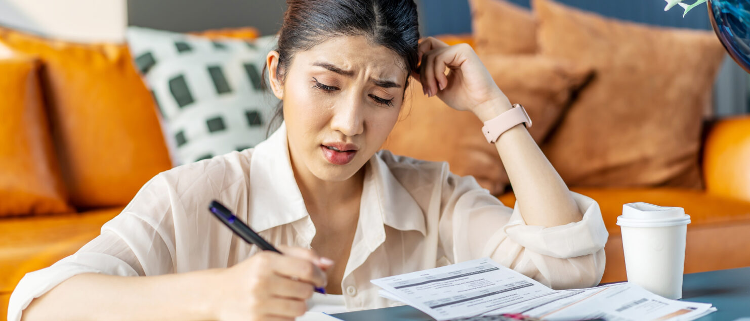 A woman looks overwhelmed while doing calculations and writing them in a notepad