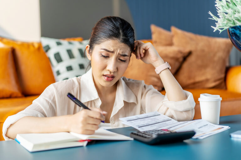 A woman looks overwhelmed while doing calculations and writing them in a notepad