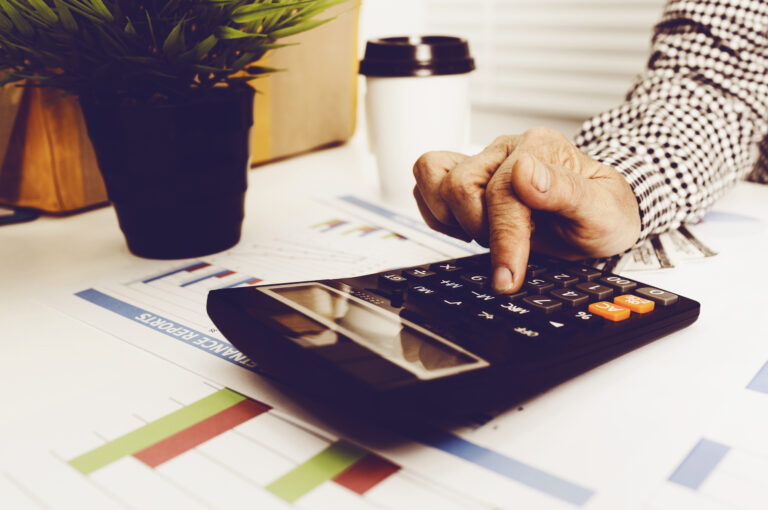 Someone types on a calculator on a desk covered in graph print-outs