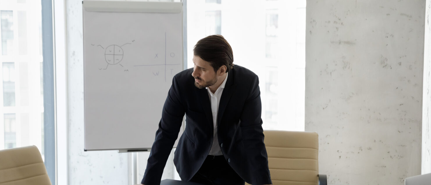 A businessman stands in an empty boardroom looking frustrated.