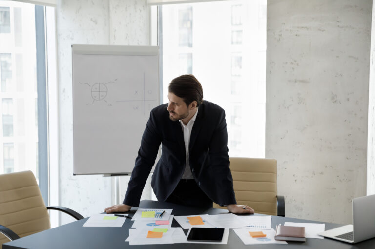 A businessman stands in an empty boardroom looking frustrated.