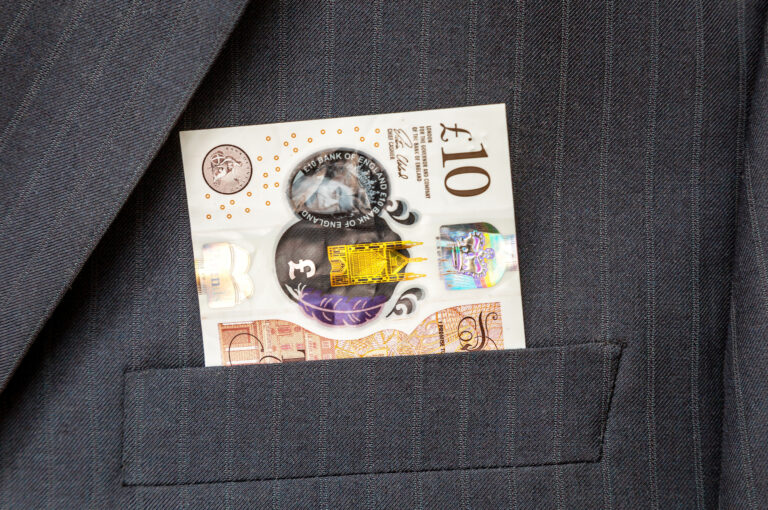 A £10 note sticks out of the pocket of a suit jacket.