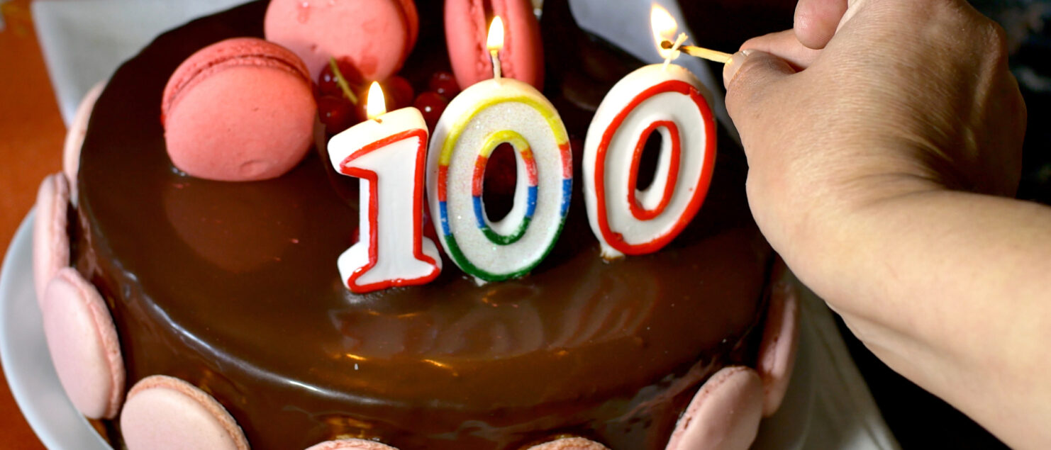 Someone lighting candles on a 100th birthday cake.