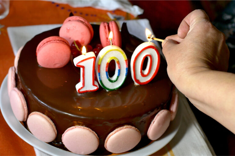 Someone lighting candles on a 100th birthday cake.
