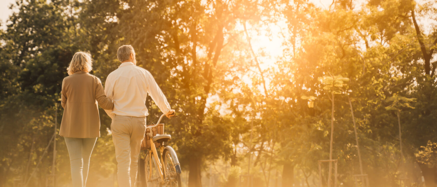 A couple walking in a park and pushing a bike.